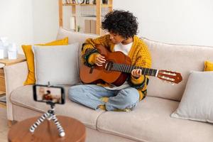 blogueur guitariste. content africain américain fille blogueur en jouant guitare en chantant chanson enregistrement vlog. social médias influenceur femme diffusion enregistrement à Accueil studio. la musique contenu créateur diffuser. photo