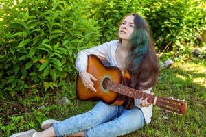 Jeune femme séance dans herbe et en jouant guitare photo