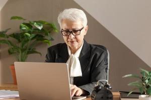 sur de soi élégant européen milieu vieilli Sénior femme en utilisant portable à lieu de travail. élégant plus âgée mature Années 60 gris aux cheveux Dame femme d'affaires séance à Bureau tableau. patron chef prof professionnel ouvrier. photo