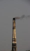 industriel brique four fermer vue avec foncé fumée à venir en dehors de le cheminée. le tuyau de un industriel brique four plante avec une foncé cendre Contexte. environnement la pollution avec une foncé brique four. photo