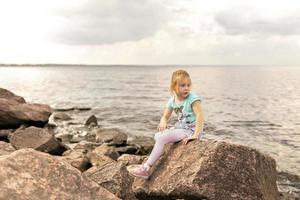 une peu fille est séance sur le rochers par le mer. golfe de Finlande. heure d'été photo