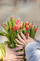 une Jeune couple dans l'amour sur le rue, en portant fleurs dans leur mains à une romantique moment. une homme donne rouge tulipes à une blond femme.la concept de le printemps vacances est Mars 8, Pâques, aux femmes journée photo
