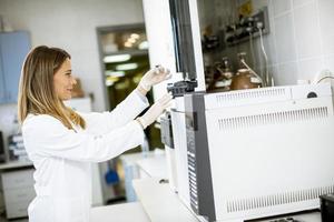 Femme scientifique dans une blouse blanche mettant un flacon avec un échantillon pour une analyse sur un chromatographe en phase gazeuse en laboratoire biomédical