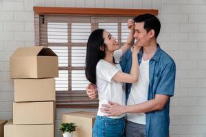 souriant Jeune asiatique content couple étreindre copain avec papier carton des boites à en mouvement journée dans leur Nouveau Accueil après achat réel domaine. concept de départ une Nouveau la vie pour une nouvellement marié couple. photo