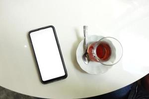 intelligent téléphone avec blanc écran et thé tasse sur table photo