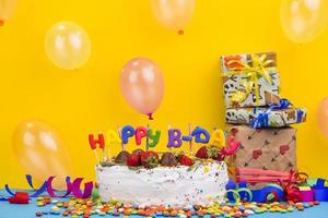 Gâteau d'anniversaire vue de face avec des cadeaux sur fond jaune vif photo