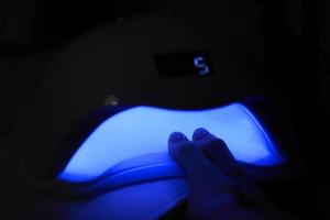 vue rapprochée des mains féminines avec manucure gel polish. une femme met la main dans une lampe uv à led pour durcir le couvercle supérieur du vernis à ongles. lampe uv, clou led photo