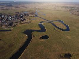 aérien vue de une magnifique enroulement rivière les flux parmi le des champs, lequel les flux pittoresquement, création incroyable paysages. entre inondé des champs et les marais. photo