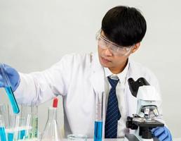 asiatique homme étudiant scientifique dans réactif mélange laboratoire dans une science recherche laboratoire avec tester tubes de divers tailles. sur le sol dans laboratoire chimie laboratoire blanc Contexte. photo