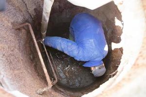 ouvrier nettoie le égout trappe.a ouvrier nettoie une égout éclore. une homme dans le éclore. photo