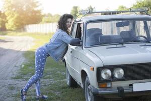 une magnifique fille habillé dans le style de le Années 90 est permanent près le vieux auto. photo