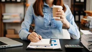 main de femme d'affaires écrivant sur le bloc-notes avec un nouveau diagramme de stratégie informatique moderne et tenant une tasse de café comme concept lumière du matin photo