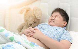 obèse garçon dans lui lit a une maux d'estomac photo