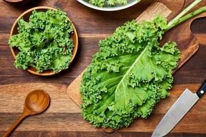 concept de Frais chou frisé feuilles salade sur en bois table Contexte. en train de préparer vert chou frisé feuilles salade nourriture dans le cuisine. plat poser, Haut vue photo