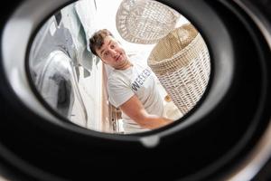 homme avec panier, vue de la lessive machine à l'intérieur. Masculin Est-ce que blanchisserie du quotidien routine. photo