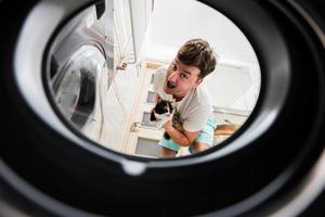 homme avec chat vue de la lessive machine à l'intérieur. Masculin Est-ce que blanchisserie du quotidien routine. photo