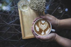 Vue de dessus de la main avec une tasse de café avec de l'art latte chaud dans un café-restaurant ou un restaurant