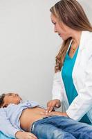médecin examiner et performant le technique de abdominal percussion à une enfant photo