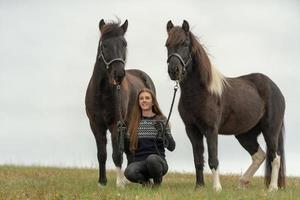 Jeune femme assise dans un champ avec ses deux chevaux islandais