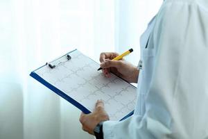 proche en haut. une magnifique asiatique femelle médecin portant une bleu infirmière uniforme. tenir une stylo et écrire quelque chose sur le presse-papiers à écrire vers le bas patient information. photo