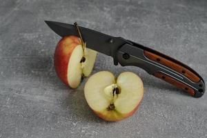 couteau pliant pour la survie et deux moitiés de pomme coupée. photo