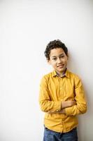 mignon petit garçon aux cheveux bouclés debout près du mur blanc photo