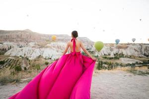 une fille dans une en volant robe avec une longue train sur le Contexte de des ballons dans cappadoce. photo