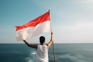 une homme en portant une rouge et blanc Indonésie drapeau à la recherche à le océan. ai généré photo