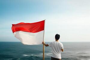 une homme en portant une rouge et blanc Indonésie drapeau à la recherche à le océan. ai généré photo