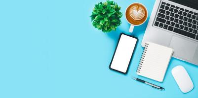 bureau avec ordinateur portable, téléphone intelligent à écran blanc, tasse de café, stylo, cahier sur fond bleu, vue de dessus avec espace de copie, maquette. photo