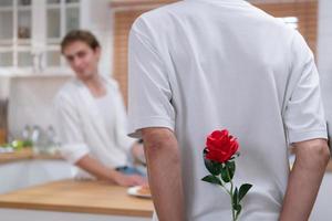 une Jeune lgbt couple fête le journée de l'amour avec une verre de du vin dans leur Accueil cuisine. avec une surprise avec une Rose de une amoureux photo