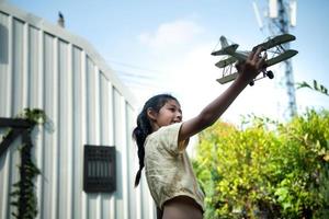 portrait de une peu fille dans le de face cour. avec modèle avion lequel est le rêver de une enfant qui veut à être une pilote. photo