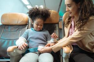 une mère assiste sa enfant dans fixation le sien ceinture de sécurité à garder lui sûr pendant une vol. photo