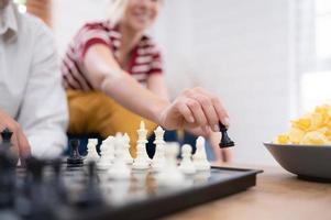 dans le vivant pièce de le loger, un personnes âgées couple est assis et se détend. à commencer en jouant échecs ensemble avec une échecs planche avec une fille applaudissement à côté de lui photo