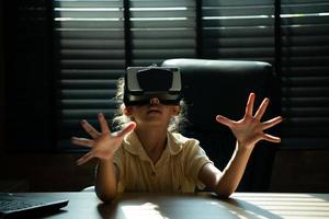 portrait de peu fille dans Bureau pièce de maison avec gestes cette sont exprimé lorsque en jouant virtuel réalité Jeux photo