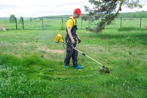 une Masculin jardinier tond le vert herbe de le pelouse dans le arrière-cour avec une de l'essence tondeuse. tondeuse pour le se soucier de une jardin terrain photo