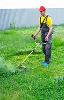 une Masculin jardinier tond le vert herbe de le pelouse dans le arrière-cour avec une de l'essence tondeuse. tondeuse pour le se soucier de une jardin terrain photo