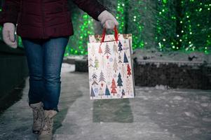 achats Sacs avec Noël modèle dans mains de une femme, en marchant vers le bas le neige couvert ville rue à hiver nuit photo