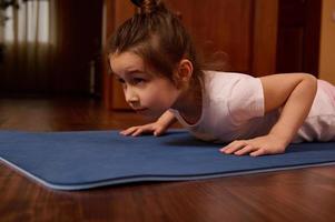 fermer caucasien 5-6 ans vieux enfant, magnifique peu fille Faire pousser en haut sur aptitude tapis à l'intérieur photo