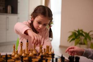 adorable 4 ans vieux peu caucasien fille cueillette en haut une échecs pièce tandis que en jouant échecs Jeu avec sa frère à maison. intelligent intellectuel planche Jeux pour enfants, logique développement, éducation concept photo