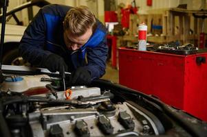 professionnel caucasien homme mécanicien dans global travail uniforme examiner réglage, fixation, réparer voiture moteur, véhicule les pièces en utilisant outils équipement dans atelier garage. soutien et voiture réparation un service photo