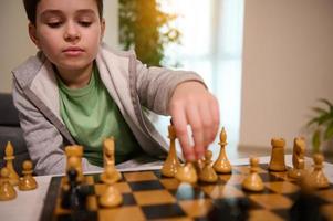 portrait de une concentré Beau intelligent garçon cueillette en haut une échecs pièce tandis que fabrication bouge toi sur échecs planche. échecs Jeu pour intelligent esprit, des gamins intellectuel divertissement et logique développement concept photo