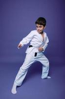 Oriental martial arts. aikido combattant, caucasien dix ans vieux garçon dans kimono améliore le sien combat compétences, isolé sur violet Contexte avec copie espace photo