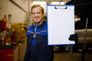 concentrer sur blanc Vide feuille avec copie un d espace sur une presse-papiers dans le main de une flou souriant technicien, voiture ingénieur, mécanicien permanent dans le garage de réparation magasin. voiture entretien concept photo