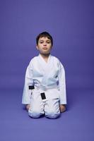 portrait de une Beau enfant garçon portant kimono et séance dans aikido position contre violet Contexte avec copie espace pour texte. Oriental martial les arts concept photo