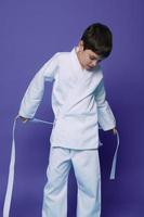 Beau enfant, caucasien adolescent garçon, aikido lutteur en mettant sur blanc kimono isolé sur violet Contexte avec copie espace pour La publicité texte photo