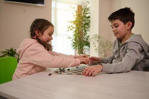 deux adorable enfants, garçon et fille, frère et sœur ayant génial temps en jouant dames table Jeu ensemble à Accueil intérieur. photo