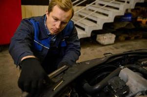 fermer de une Jeune caucasien mécanicien dans voiture un service ajustement phares sur voiture dans le réparation magasin garage. auto service, voiture réparation et garantie entretien concept photo