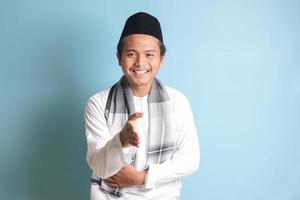 portrait de attrayant asiatique musulman homme dans blanc chemise atteindre en dehors le sien main pour une poignée de main, accueillant quelqu'un. isolé image sur bleu Contexte photo