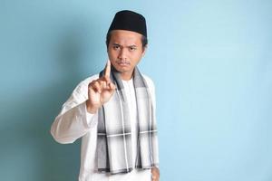 portrait de Jeune asiatique musulman homme montrer du doigt en haut le sien index et rappelant quelque chose à faire. La publicité concept. isolé image sur bleu Contexte photo